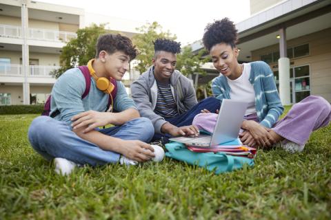 3 students on grass with laptop